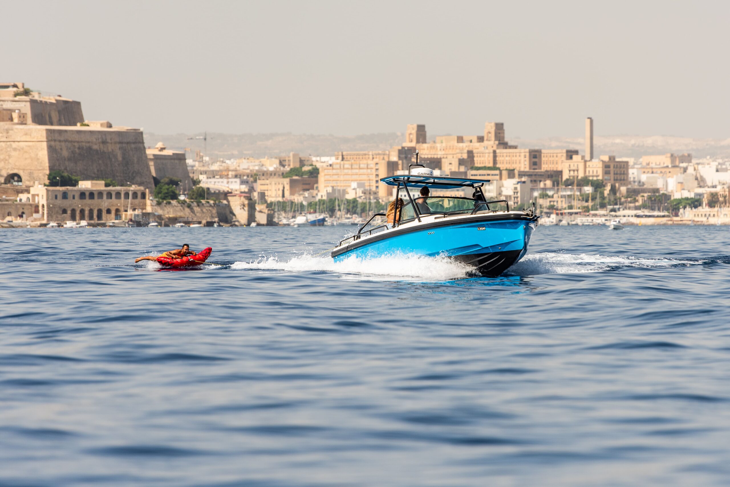 Sport boat with a tow tube running past the Valletta skyline