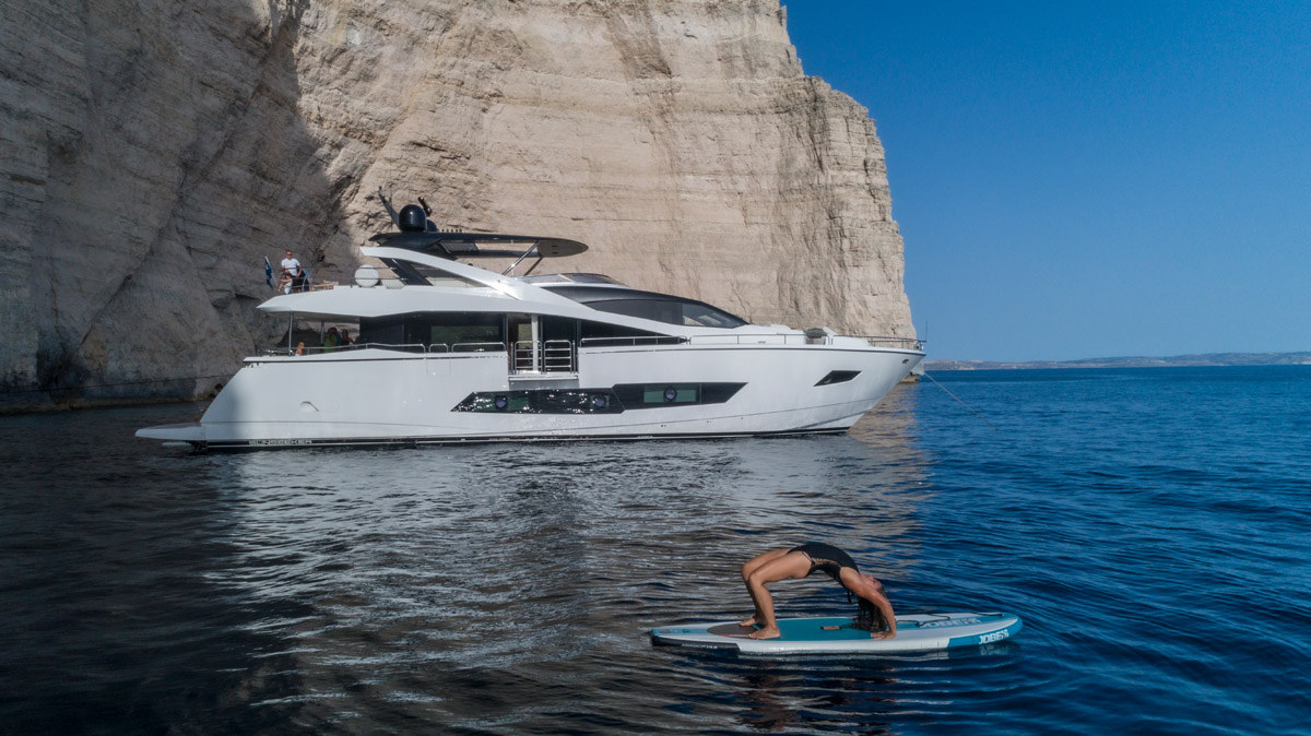 Yacht beside a Maltese cliff with a paddleboarder in the foreground