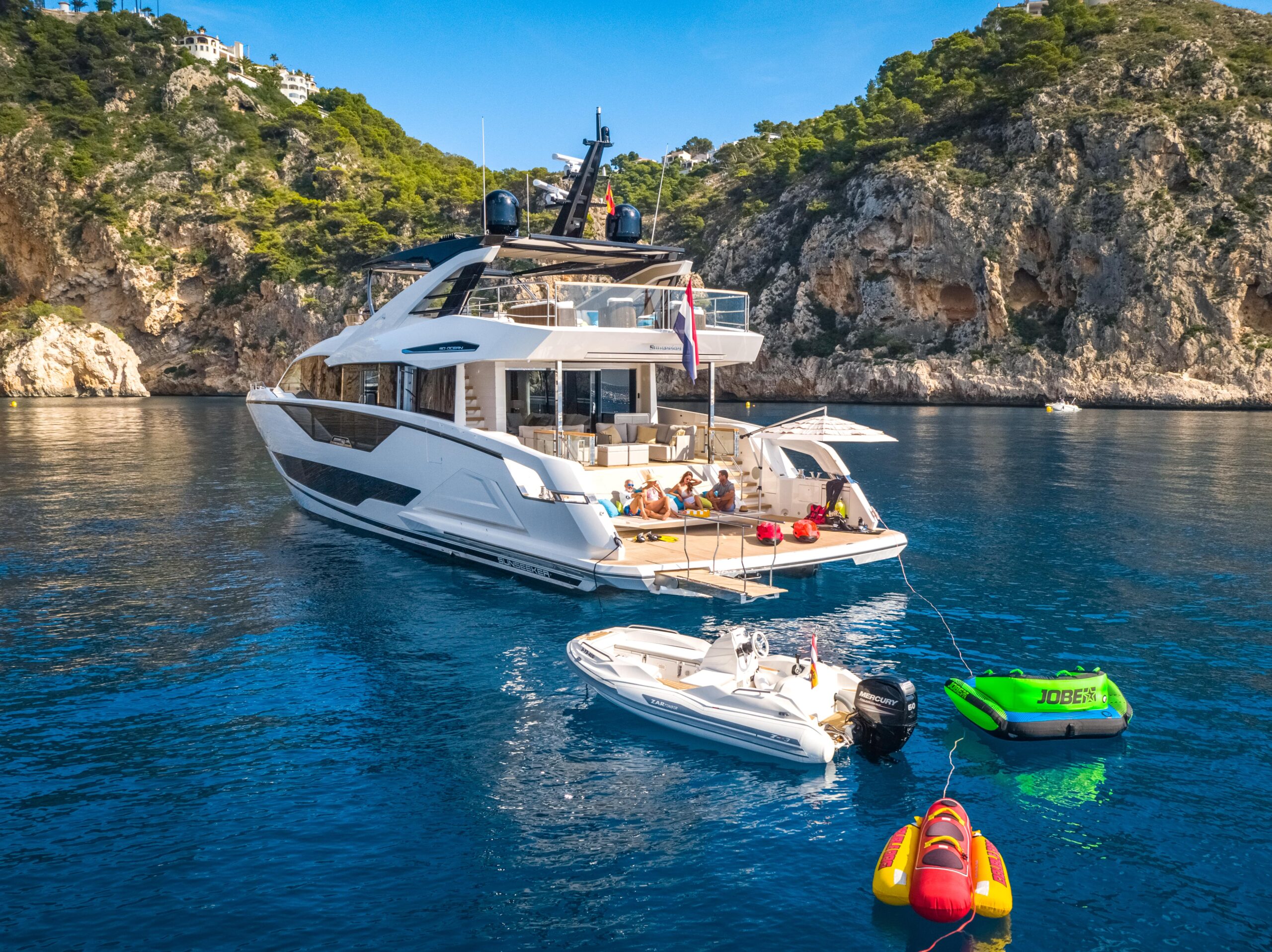 Yacht anchored in a cove with tender and inflatable toys in the water